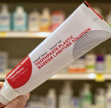 Mano sosteniendo un pequeño tubo blanco con etiqueta roja, con estantes de tienda desenfocados al fondo.