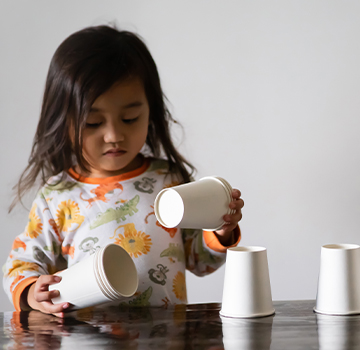 child with blurred face stacking white paper cups on a table