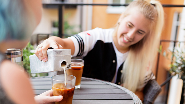 Woman pouring coffee into a glass at an outdoor café.