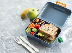 Bento: sándwich, verduras, frutos secos, uvas; plátano y botella de agua al lado